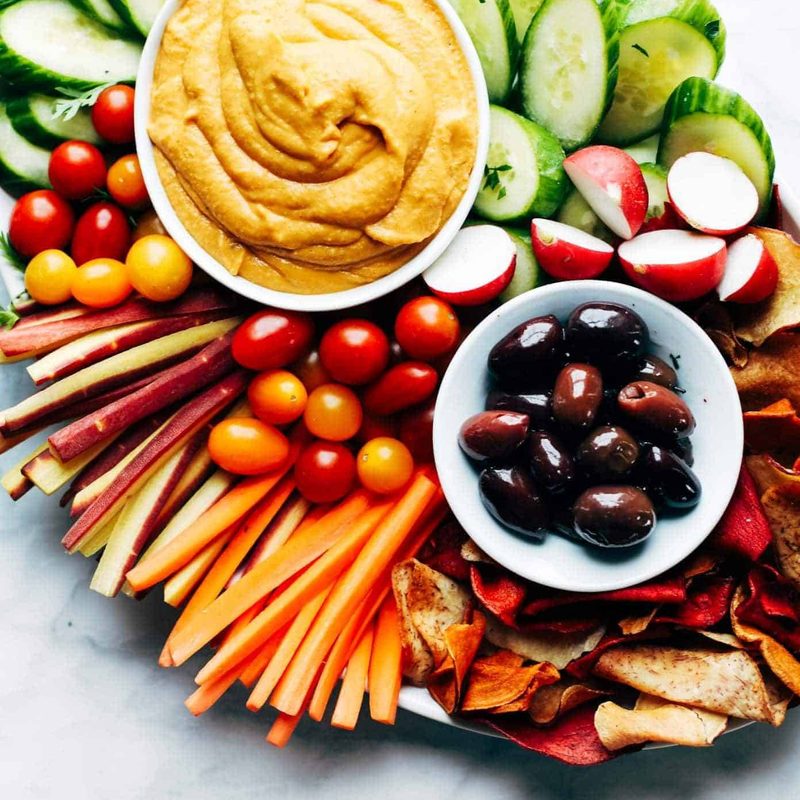 Plates of hummus and olives on a pile of vegetables.