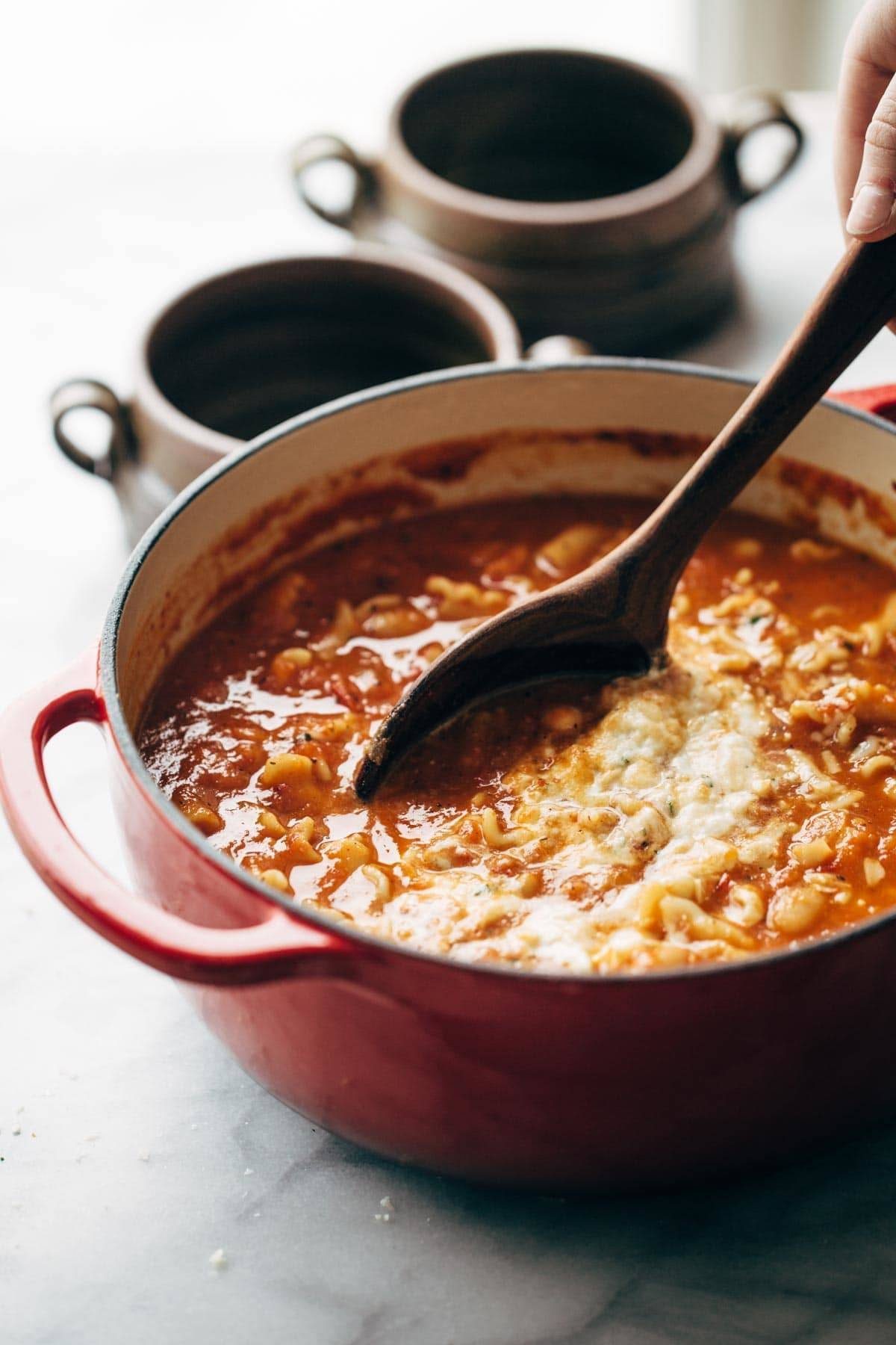 Roasted Garlic and White Bean Lasagna Soup in a red dutch oven with a wooden spoon.