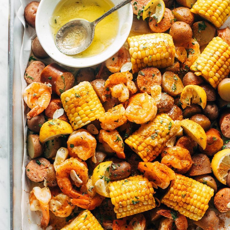 Shrimp, potato and corn mixture on a sheet pan with a side of melted butter in a bowl.