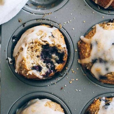 Whole Wheat Blueberry Muffins in a muffin tin with glaze.
